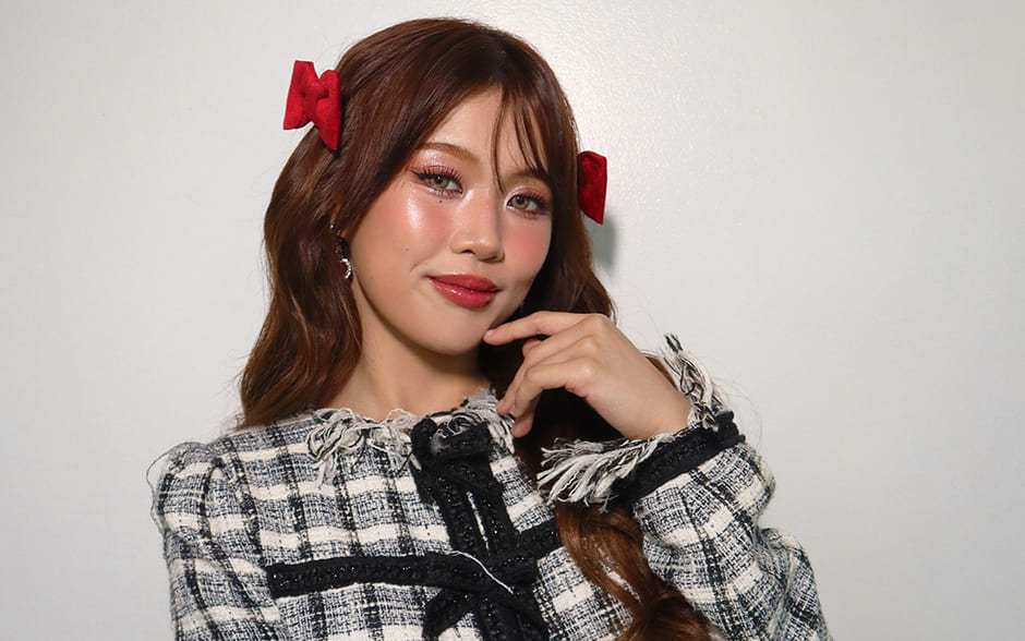 BINI Maloi posing elegantly in a chic plaid outfit with fringe details, accessorized with red hair bows.