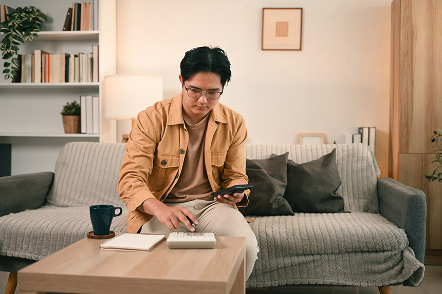 Person using a calculator and smartphone to review expenses at home.