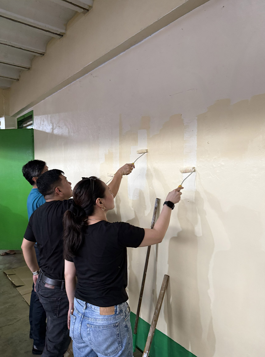 Globe employee volunteers repaint a school wall using paint rollers during Brigada Eskwela 2026.